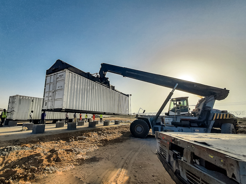 A crane lifts a large, white container into the air