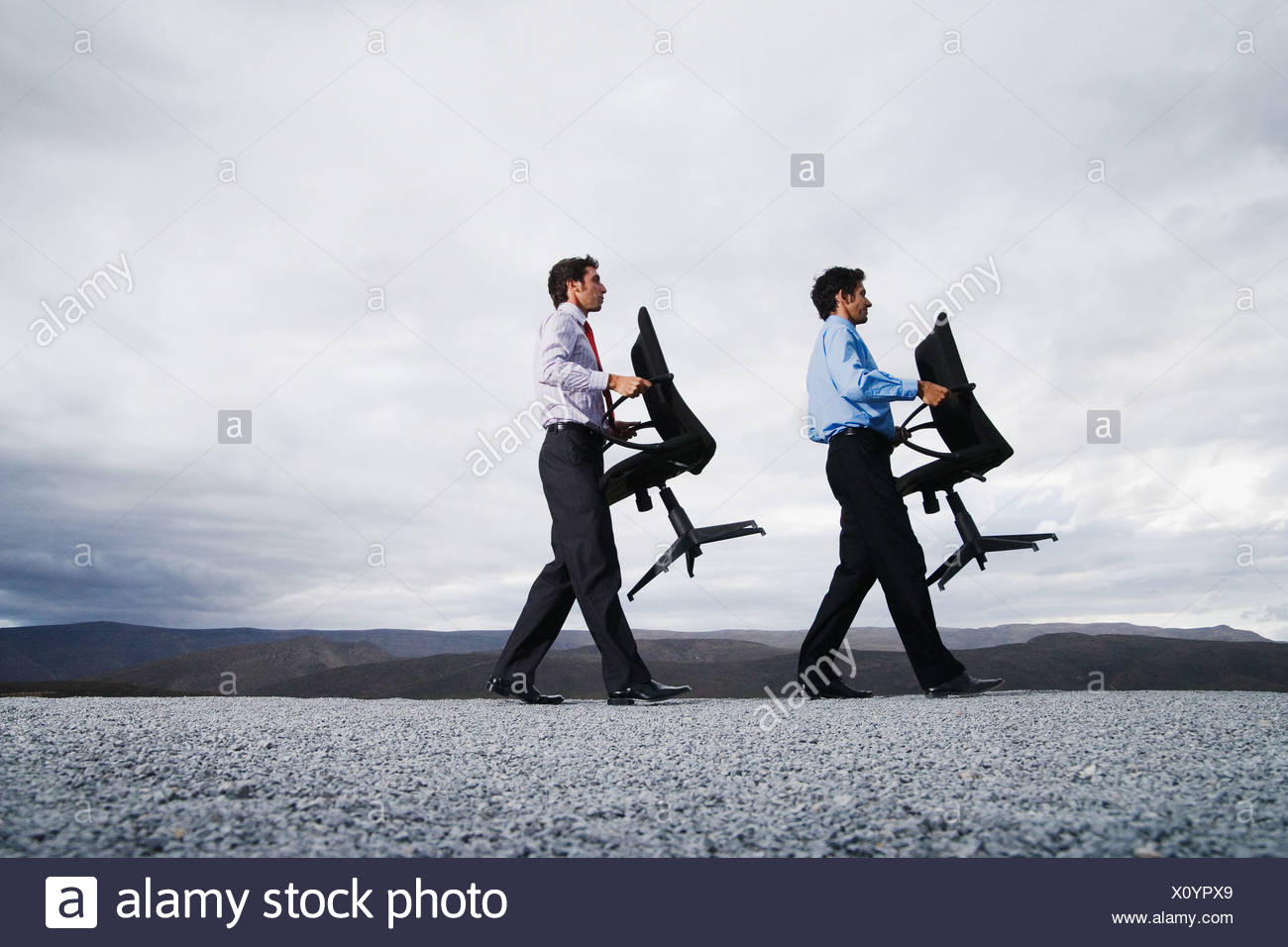 two-men-carrying-office-chairs-outdoors-X0YPX9.jpg