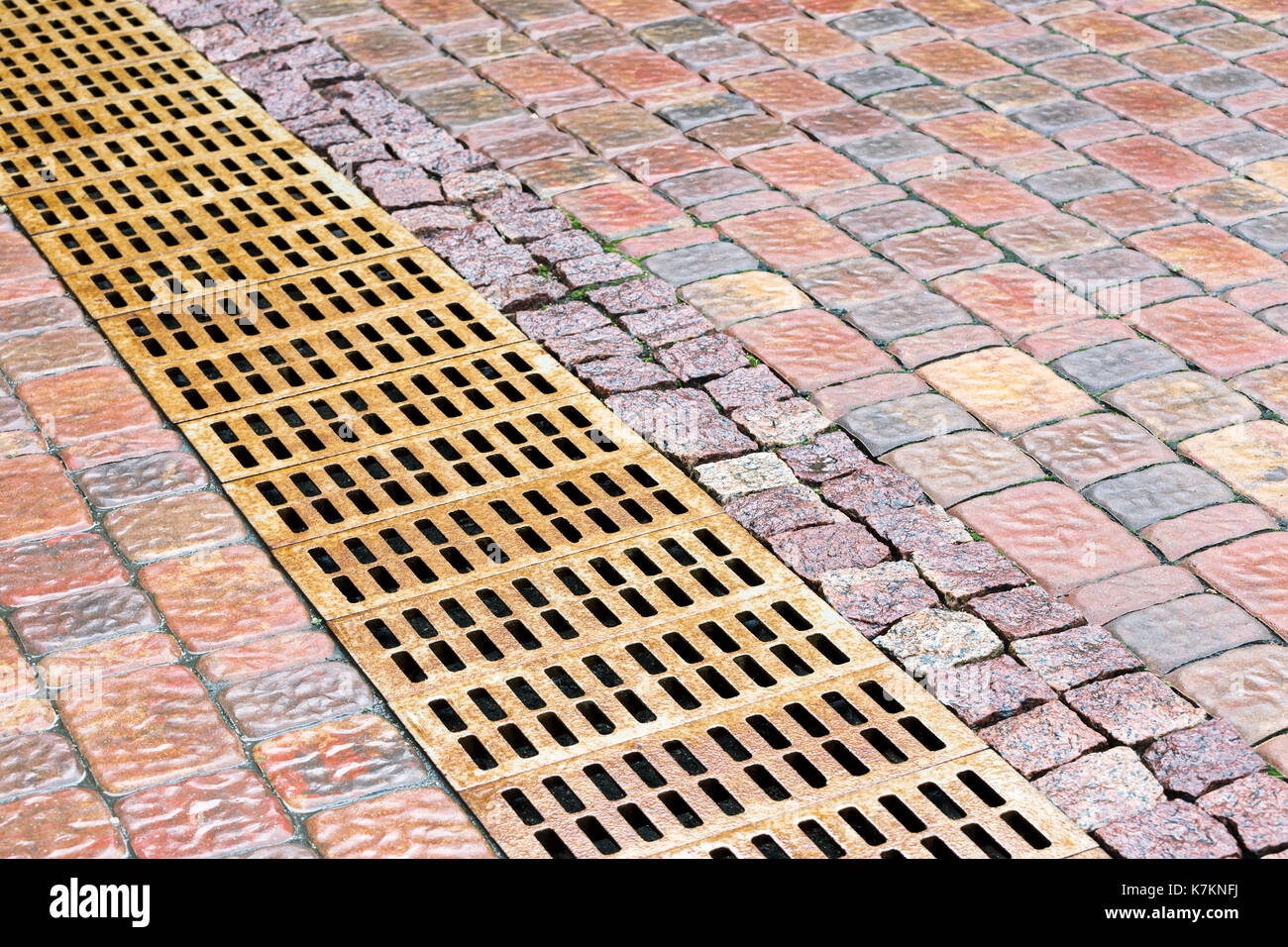 rusty-metal-sewer-grate-for-drainage-system-on-wet-cobblestone-sidewalk-K7KNFJ.jpg