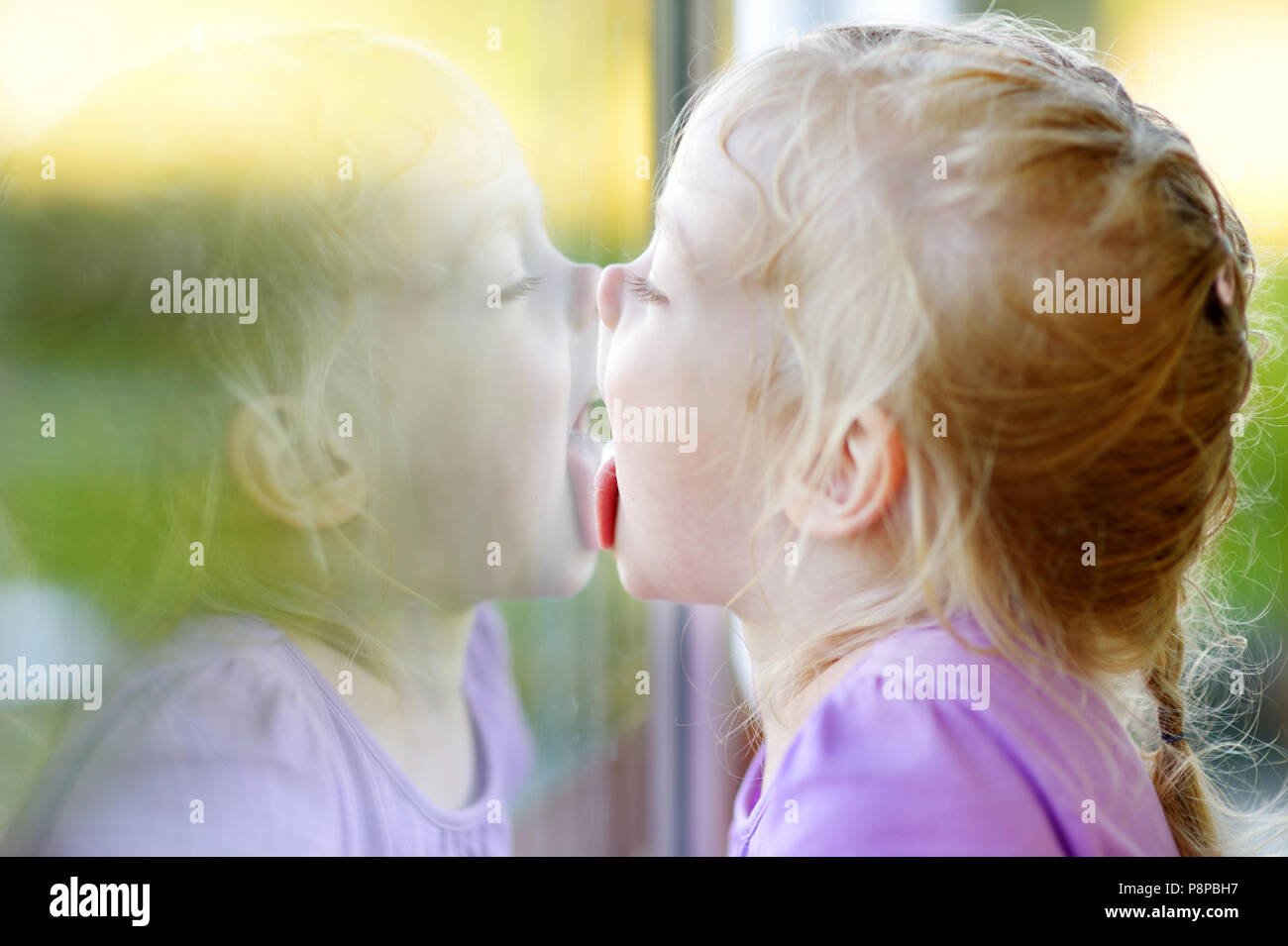 cute-funny-little-girl-licking-her-reflection-on-a-window-glass-P8PBH7.jpg