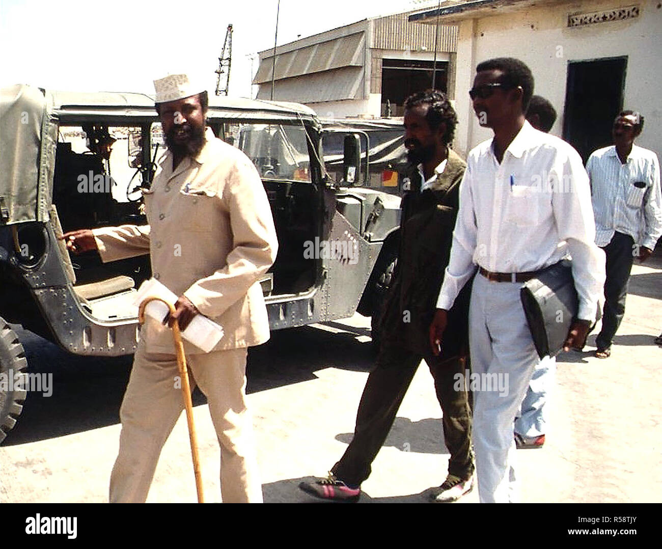 1992-straight-on-shot-of-somali-faction-leader-col-jess-at-left-with-hat-and-cane-walking-outside-the-joint-task-force-headquarters-in-kismayo-somalia-with-his-entourage-he-had-just-completed-a-meeting-with-bgen-lawson-magruder-usa-joint-task-force-commander-in-kismayo-bgen-magruder-not-shown-is-from-the-10th-mountain-division-fort-drum-new-york-this-mission-is-in-direct-support-of-operation-restore-hope-R58TJY.jpg