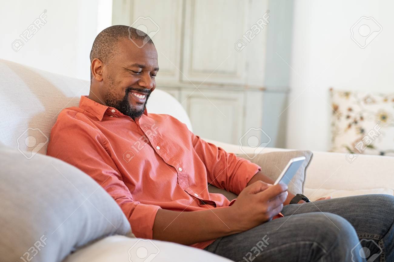 124982703-happy-black-man-using-smart-phone-while-relaxing-at-home-smiling-mature-man-at-home-sitting-on-couch.jpg